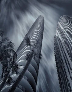 Modern skyscrapers with palm trees under a cloudy sky in Miami.